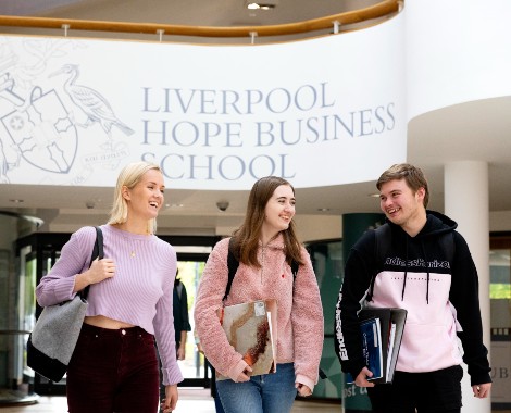 Two male students and a male student walking through a corridor with a Liverpool Hope Business School sign overhead.